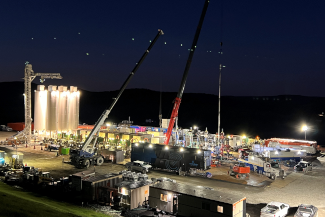 Night scene of a well-lit industrial site with cranes, silos, and equipment against a dark sky.